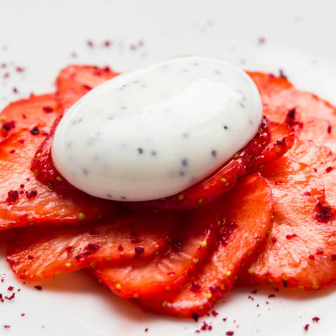 A yoghurt and honey sphere placed on top of thinly sliced strawmberries. 