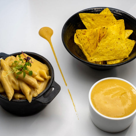 Image shows 3 cheesy dishes, a white pot filled with Creamy Vegan Cheese Sauce with Nachos to dip, a black pot filled with Mac & Cheese. 